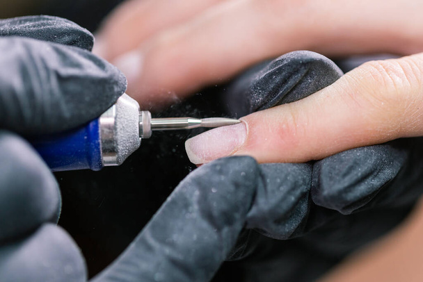 Vrouw gebruik elektrische nagel bestand boor in schoonheidssalon. Nagels manicure proces in detail. Gel polish close-up concept. - Foto, afbeelding