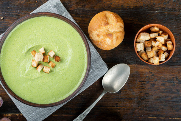 green broccoli cream soup in a plate on the table. next to them are fresh buns. the soup is decorated with cracker - Φωτογραφία, εικόνα