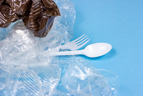 Cucharas de plástico triturado, tenedores, botellas y tazas como un desperdicio desechable sobre fondo azul brillante. Concepto de contaminación ambiental y reciclaje de basura
. - Foto, Imagen