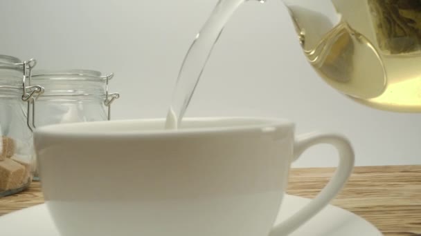 Χύνοντας λευκό αυθεντικό τσάι σε κλασικό λευκό κύπελλο στο ξύλινο τραπέζι - Πλάνα, βίντεο
