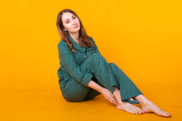Smiling young girl in pajamas home wear posing while resting at home isolated on yellow background studio portrait. Relax good mood lifestyle concept. - Foto, Imagem