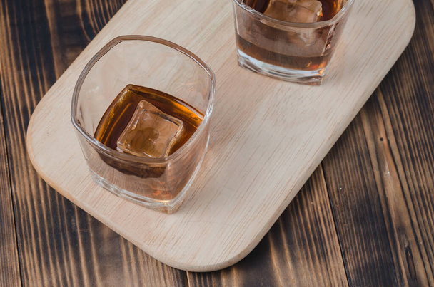 Two Glasses of cognac with ice cubes on a wooden table/Two Glasses of cognac with ice cubes on a wooden table. Top view - Фото, изображение