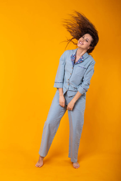 Glimlachend jong meisje in pyjama 's thuis poseren terwijl thuis geïsoleerd op gele achtergrond studio portret. Relax goed humeur lifestyle concept. - Foto, afbeelding