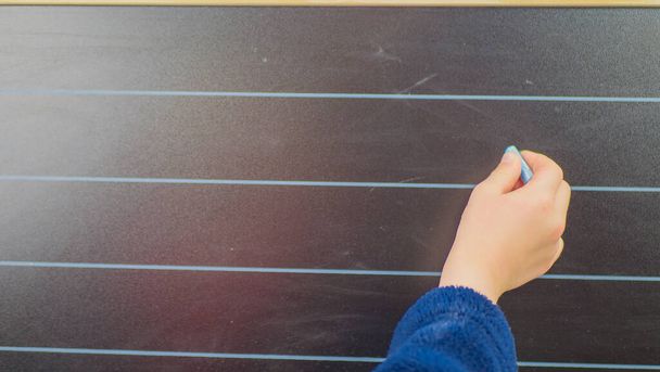 schoolboy hand writes in chalk on a blackboard during a lesson at schoo. - Photo, Image