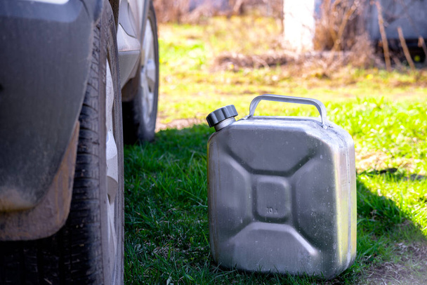 Ein Metallkanister mit Benzin steht auf dem Gras neben dem Auto. Dem Auto ging das Benzin aus. Betanken eines Autos mit Gas aus einem Kanister. Aluminiumbrennstoffkanister - Foto, Bild
