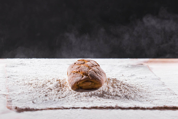Traditional artisan rye bread loaf fall into flour. Dark background. Bakery and homemade rustic bread concept. - Fotó, kép