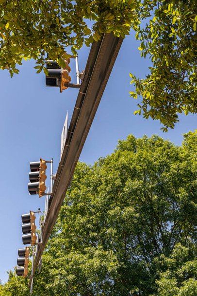 Row of stoplights on a traffic arm, seen from below, blue sky and green trees, vertical aspect - Photo, Image