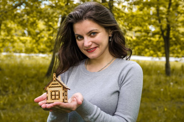 όμορφη νεαρή κοπέλα με ένα ξύλινο σπίτι στα χέρια της. Κοντινό πλάνο. - Φωτογραφία, εικόνα