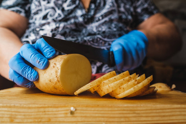 Vanhempi nainen leikkaa perunoita syödäkseen hanskoillaan. - Valokuva, kuva