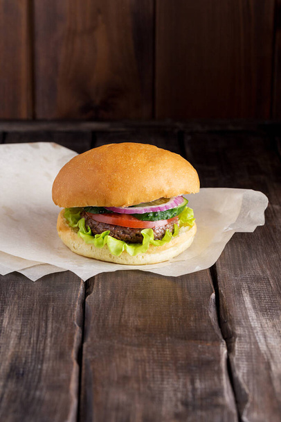 Čerstvý domácí hamburger s hovězím masem, rajčaty, salátem, okurkou a cibulí na tmavém dřevěném stole. Koncept fast food na tmavém pozadí s místem pro váš text. - Fotografie, Obrázek