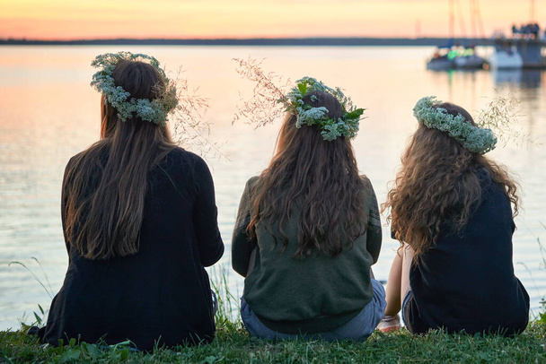 Three girls with wreaths of wild flowers by the lake. An evening at Saint John's Eve by the lake. Midsummer folk festival in Lithuania - Photo, Image