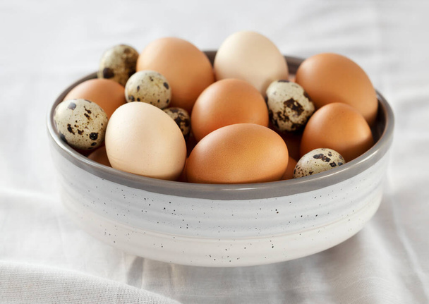 Výběr kuřecích a křepelčích vajec v misce na stole s bílou látkou. - Fotografie, Obrázek