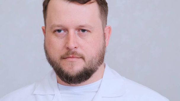 γενειοφόρος άντρας γιατρός με άσπρα ρούχα που δείχνει λυπημένος κουρασμένος βλέμμα. - Φωτογραφία, εικόνα