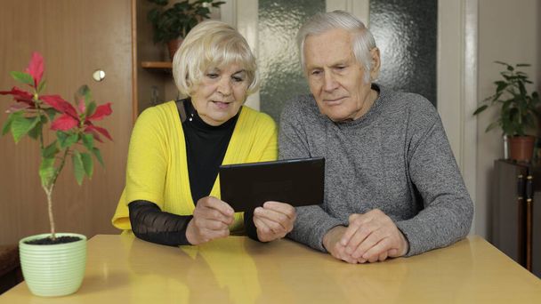 かなり成熟したシニアカップル祖父母は自宅でタブレットでオンラインショッピングを楽しむ - 写真・画像