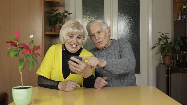Pretty mature senior couple grandparents enjoy online shopping on phone at home - Photo, Image