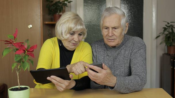 Довольно зрелая пожилая пара бабушка и дедушка наслаждаются онлайн покупки по телефону, планшету
 - Фото, изображение