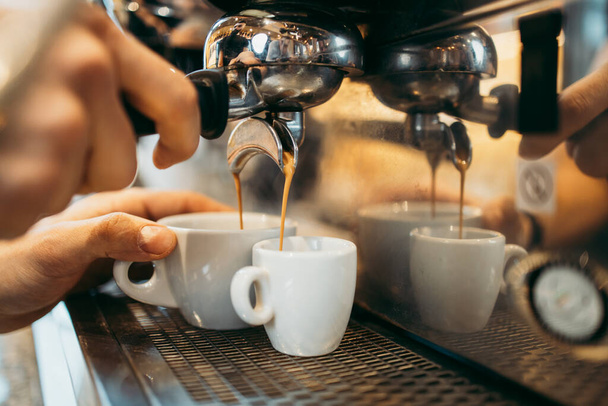 Close up shot of experienced barman or bartender hands making delicious and fresh espresso coffee drink on machine. - Foto, imagen
