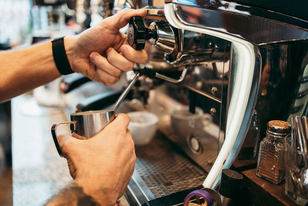 Close up shot of experienced barman or bartender hands making delicious and fresh espresso coffee drink on machine. - Foto, afbeelding