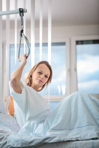 Pretty, young, female patient in a modern hospital room. Getting better fast after a surgery - pensive yet positive, thinking ahead, making plans (shallow DOF; color toned image) - Фото, изображение