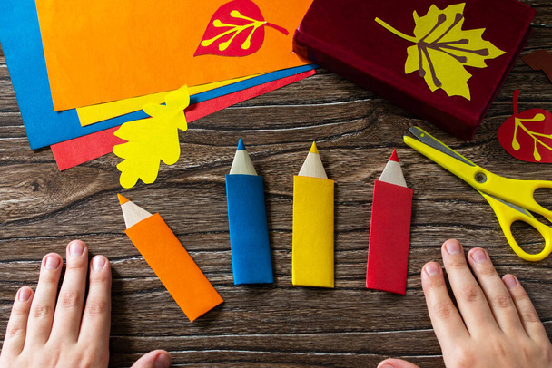Child holds multi-colored bookmarks origami pencil made of paper new school year on a wooden table. Welcome to school. Children's art project, needlework, crafts for children. - Photo, Image
