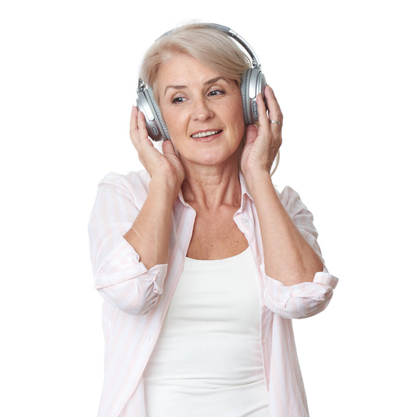 Beautiful senior blonde woman is listening to music in wireless headphones isolated on white background - Foto, Imagen