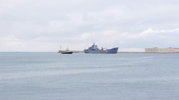 Ένα πολεμικό πλοίο συνοδευόμενο από ρυμουλκό εισέρχεται στον κόλπο. Συννεφιασμένος ουρανός - Πλάνα, βίντεο