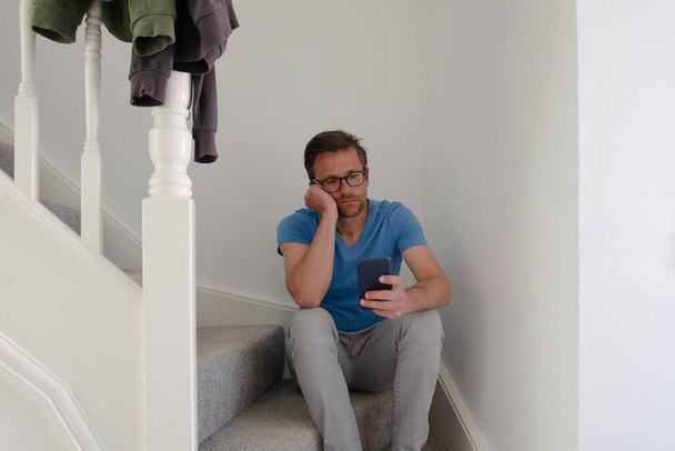 Ο άνθρωπος που κάθεται στις σκάλες κοιτάζοντας το τηλέφωνο με δυστυχισμένη έκφραση  - Φωτογραφία, εικόνα