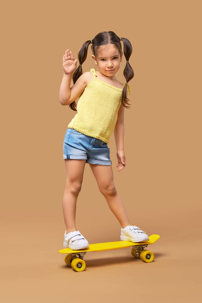 Active young girl on skateboard showing hello sign - Fotoğraf, Görsel