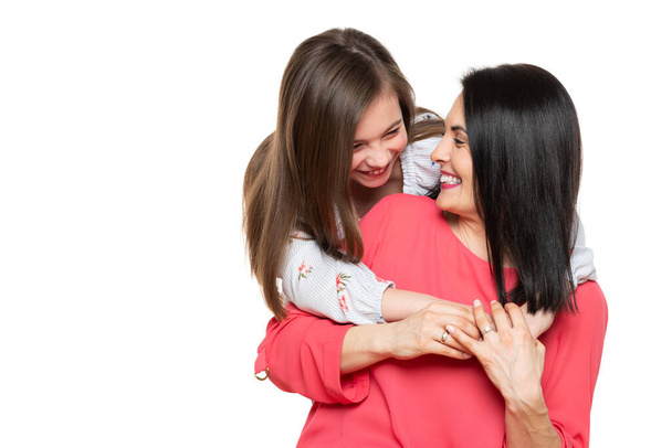 Waist up studio portrait of cute and playful schoolgirl embracing her mother. Happy family laughing background isolated over white. - Photo, Image