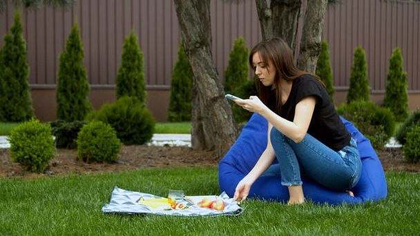 Fiatal nő fényképezés gyümölcsök és szendvics a kertben - Fotó, kép