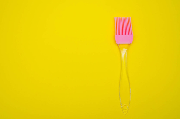 Silicone brush for lubrication on a yellow background. Pink brush with transparent pen. Top view, from the first person. Macro - Foto, Imagem