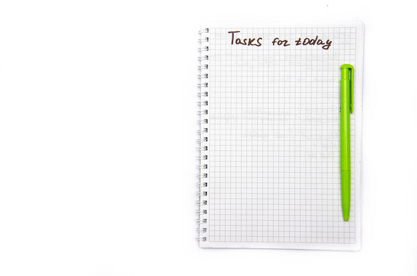 Notebook with a spiral in a cage on a white background. Top notepad contains tasks for today with a black marker, pen. Notebook top view, green pen on black - Photo, Image