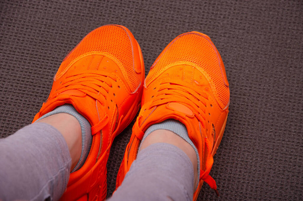 Female legs in gray sweatpants, leggings in bright orange sneakers for sports, jogging, fitness with high soles on gray Karimat. Female legs in orange sneakers on a gray mat for yoga, sports, tourism - Photo, Image