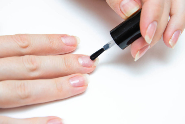 Manicure at home, during quarantine. Home manicure. The girl applies a transparent varnish, cuticle oil, nails on a white background with a brush on the nail. Macro - Foto, Imagen