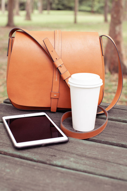 Stylová dámská taška, šálek kávy (čaje) a iPad na dřevěném stole v parku. Koncept životního stylu - Fotografie, Obrázek