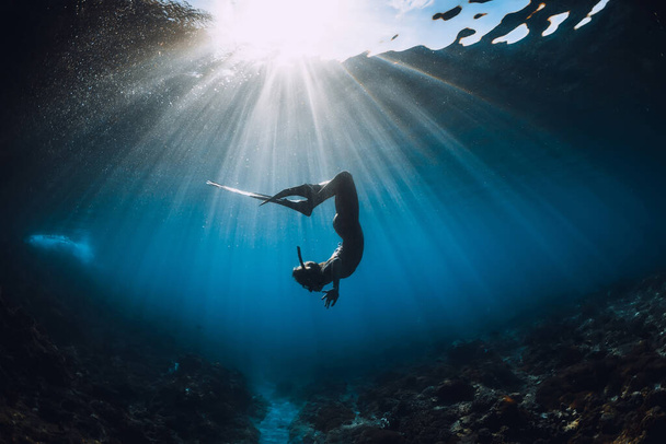 Free diver woman with fins glides over coral bottom and amazing sun rays. Freediving underwater in ocean - Photo, Image