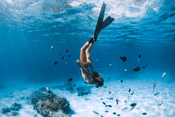 Buzo libre chica con aletas se desliza sobre fondo arenoso con peces tropicales en el océano azul
 - Foto, imagen