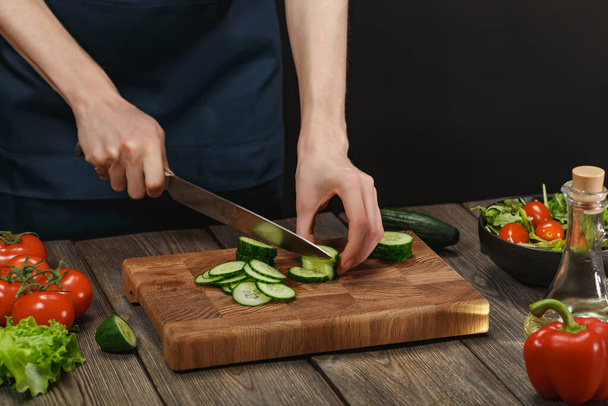 Woman cooking fresh healthy salad. Female hands cutting vegetables on board on wooden table with copyspace. - Фото, изображение