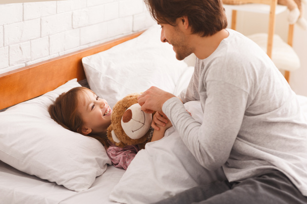 Little girl lying in bed in morning, hugging teddy bear - 写真・画像