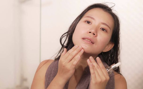 young happy and beautiful Asian Korean woman applying moisturizer facial cream and beauty treatment at home bathroom in morning routine smiling cheerful and fresh - Φωτογραφία, εικόνα