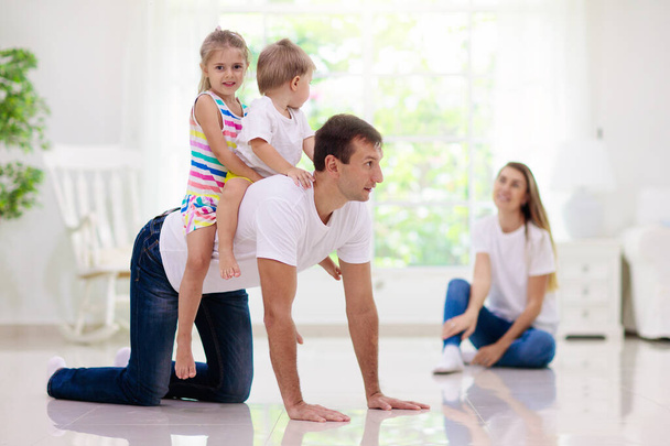 Happy young family with kids at home. Father, mother, daughter and son playing on the floor in living room. Mom, dad, little boy and girl holding pet cat. Parents and children play together. - Foto, afbeelding