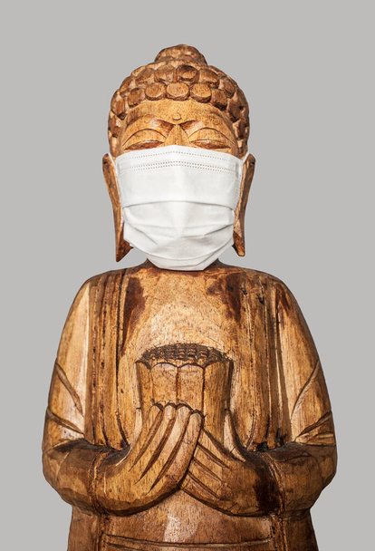 Boeddha houten standbeeld met gezichtsmasker. Geïsoleerd over grijs. Covid-19-concept - Foto, afbeelding