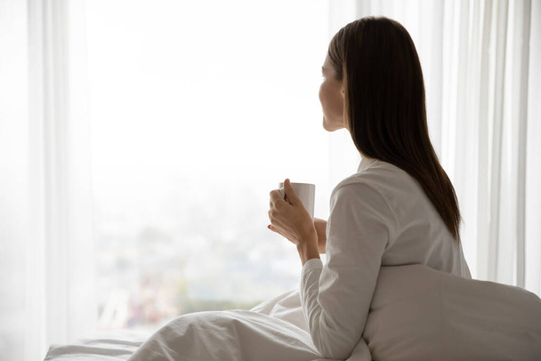 Женщина проснулась сидя на кровати, держа чашку с чаем
 - Фото, изображение