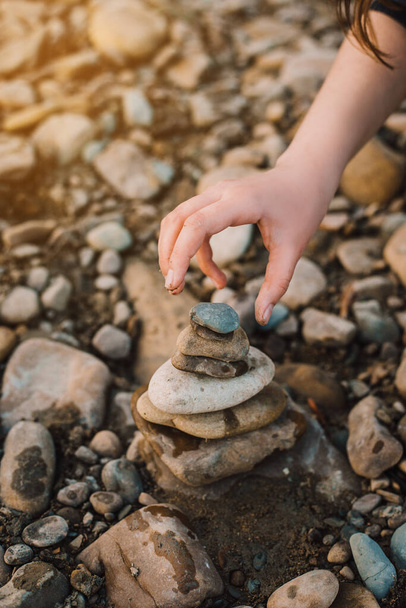 Kiegyensúlyozott kőpiramis az óceán partján hajnalban. Tengeri kavicsok torony közelsége szimbolizálja a stabilitás, a harmónia és az egyensúly. A gyerek egy piramist épít kövekkel. - Fotó, kép