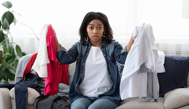 Shocked black girl sitting at home surrounded by lots of clothes - Photo, Image