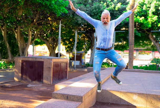 Lächelnder Senior entspannt sich im Park. Reifer Mann hat Spaß und springt wie ein Kinder.- Fokus auf dieses Gesicht - Imagen - Foto, Bild