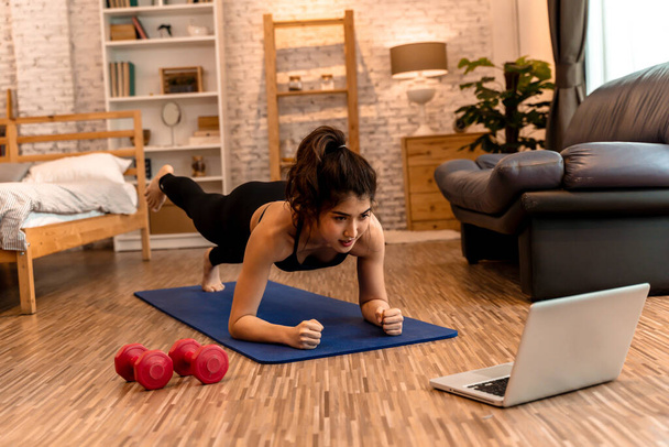 20s young Asian woman in sportswear doing plank poses while watching fitness training class on computer laptop online. Healthy girl exercising and learning in bed room. Internet education concept - Foto, Bild