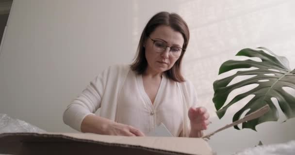 Woman packing parcel cardboard box on table at home, in office, and leaves frame - Кадри, відео