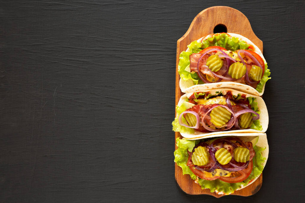 Bacon casalingo Cheeseburger Tacos su una tavola di legno rustico su una superficie nera, vista dall'alto. Posa piatta, sopraelevata, dall'alto. Copia spazio
. - Foto, immagini