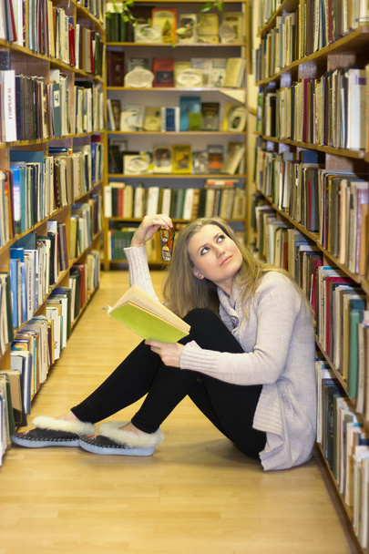 Tyttö istuu lattialla vanhassa kirjastossa
 - Valokuva, kuva